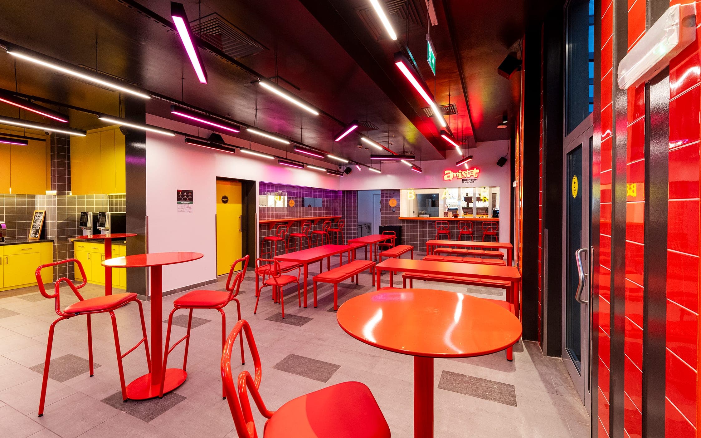 Dining room seen from the bar side, red tables and yellow kitchen
