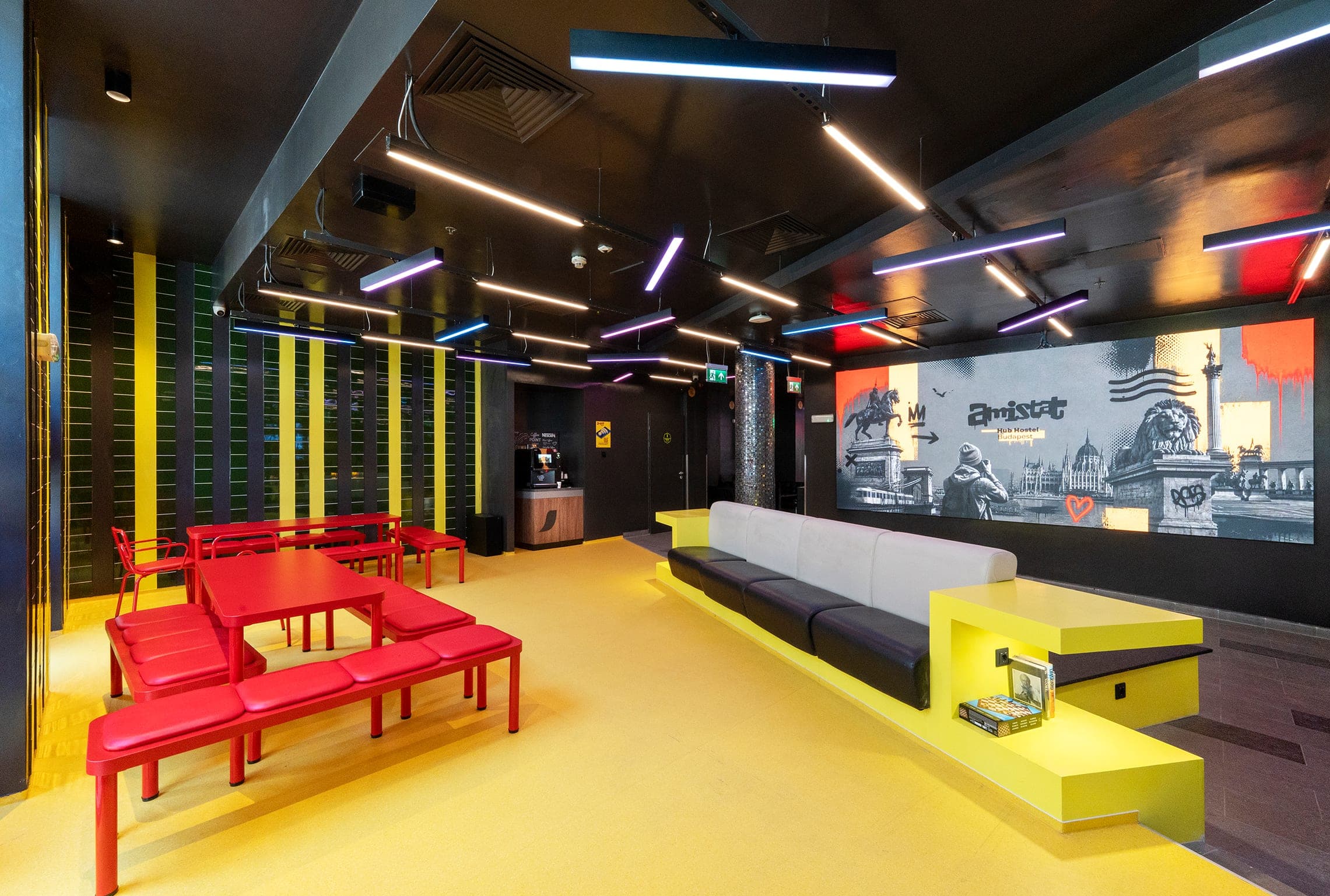 Lounge with red tables, yellow bench and a screen wall