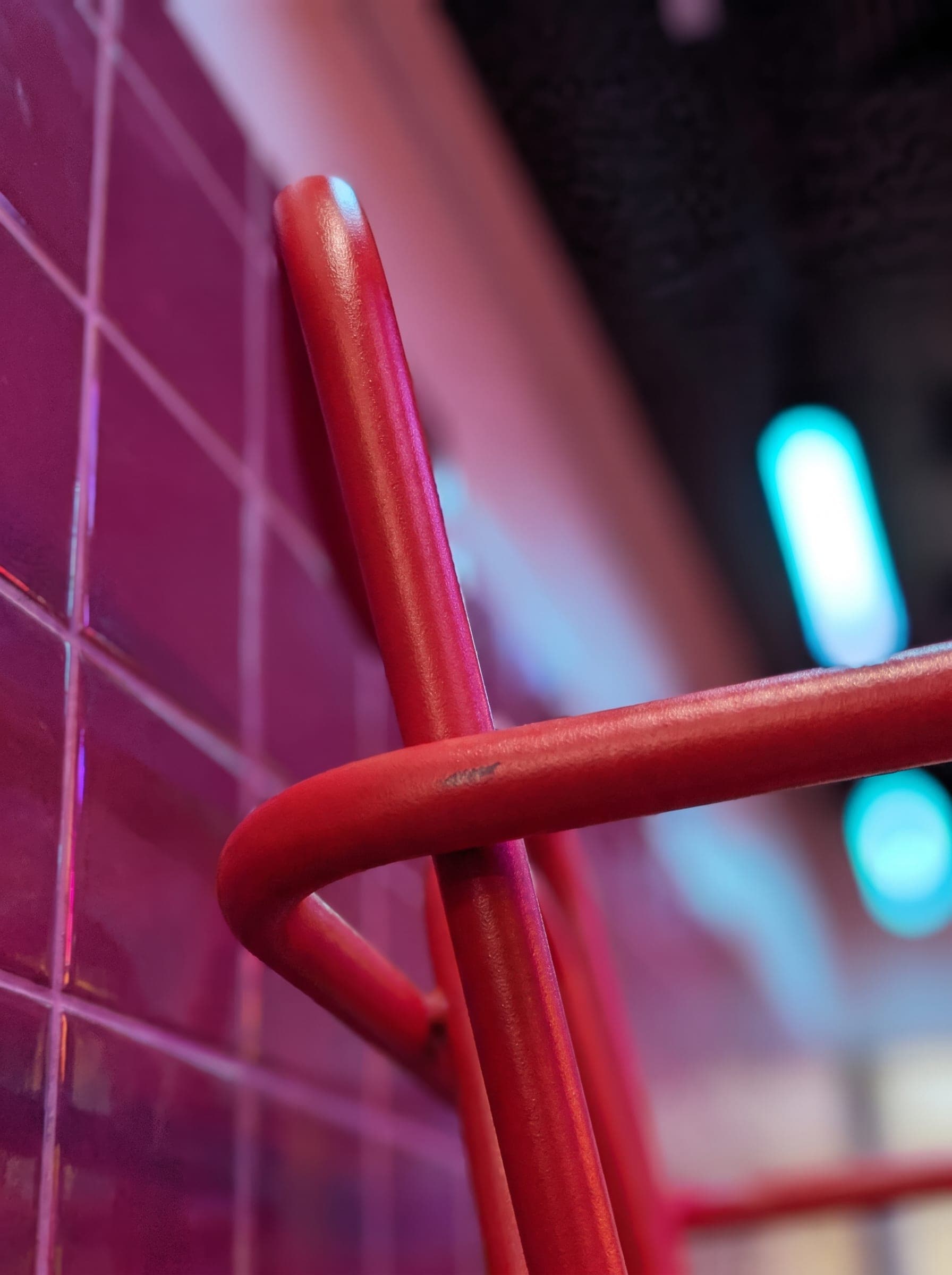 Red rail against magenta tile under a cyan tube