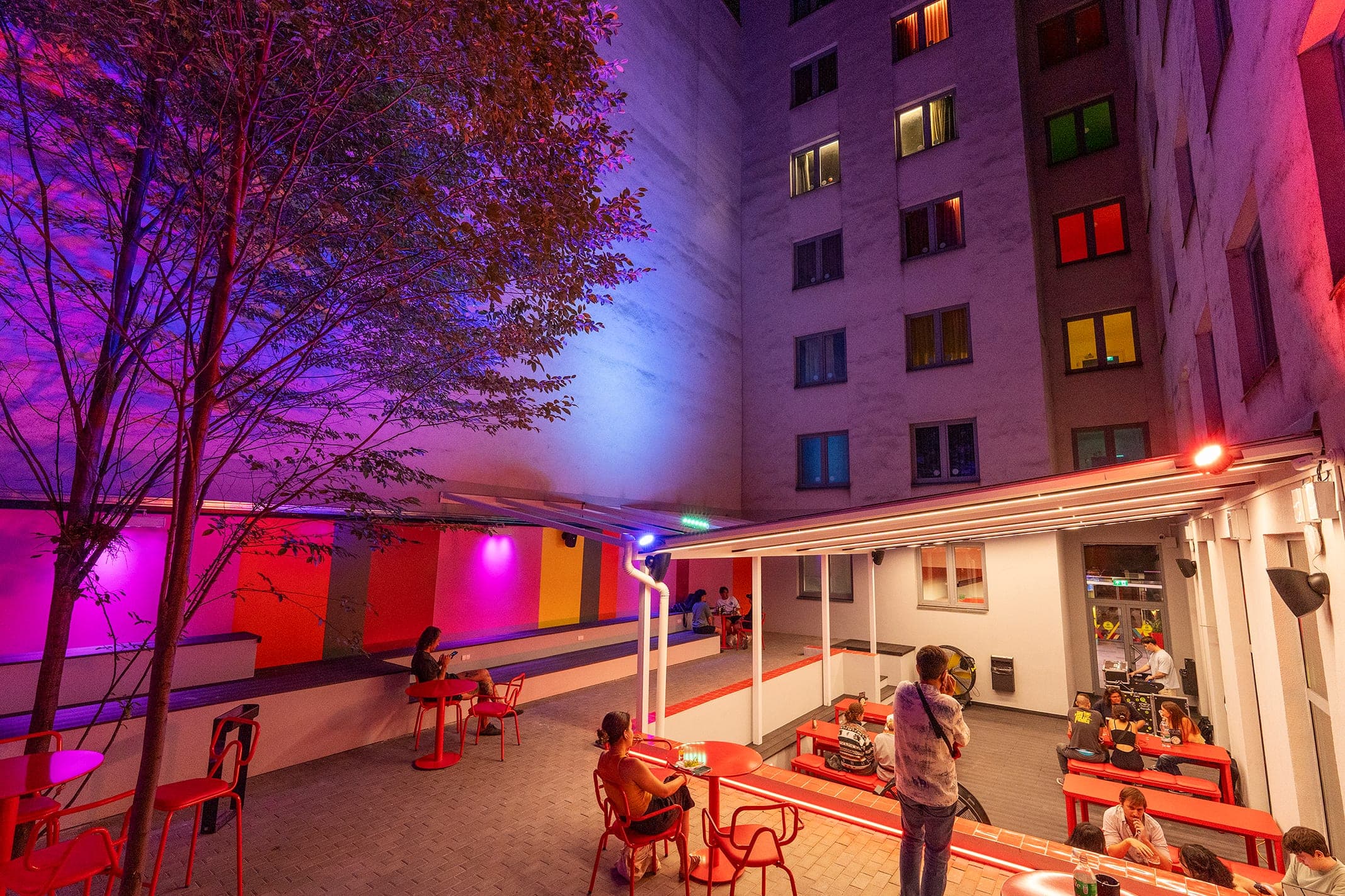 Courtyard terrace at night, lit walls and guests at red tables